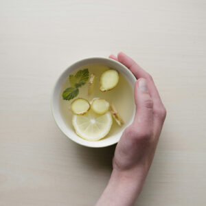 A hand holding a cup of ginger, mint and lemon tea